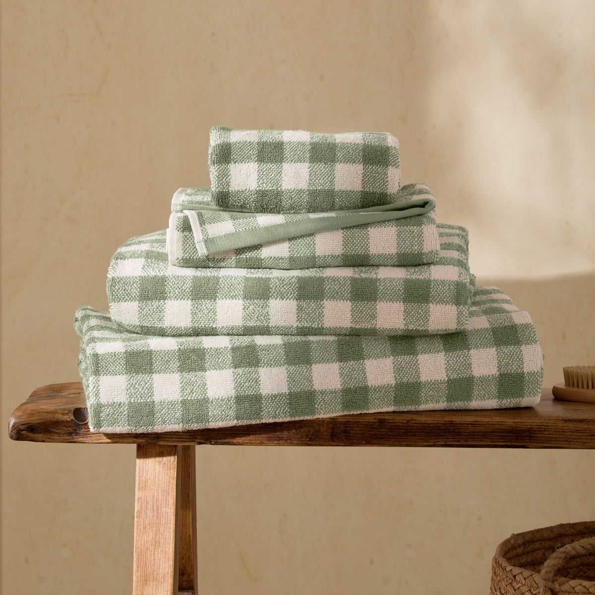 Stack of Barton Gingham Cotton Towels in Forest, showing face cloth, hand towel, bath towel and bath sheet in green and white check, on a wooden bench.