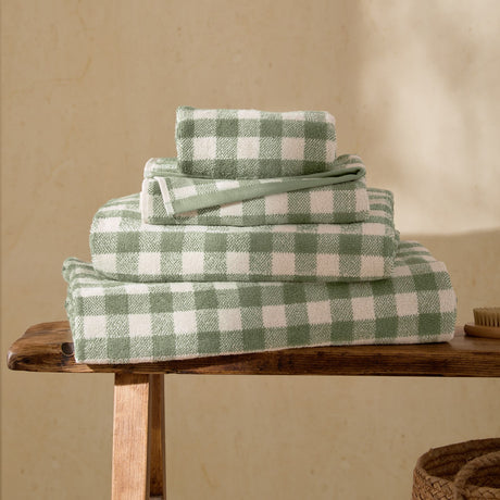 Stack of Barton Gingham Cotton Towels in Forest, showing face cloth, hand towel, bath towel and bath sheet in green and white check, on a wooden bench.