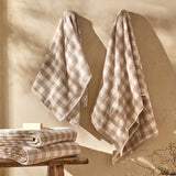 Barton Check Gingham Cotton Towels in natural and cream hung on wall hooks in a bathroom, with a folded stack and soap bar on a wooden stool below.
