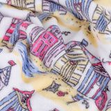 Close-up of the Beach Huts Printed Polyester Throw, rumpled fleece fabric showing illustrated beach huts in pink, blue, yellow and lilac on a cream background.