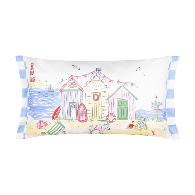 Rectangular polyester cushion with a hand-painted beach scene featuring colourful huts, a lighthouse, sailing boat, bunting and a dog on sand, blue-and-white striped side trim, on a white background.