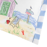 Close-up of the Beach Huts Gingham polyester cushion showing a hand-painted seaside scene with a pink beach hut, deckchair, bucket, lobster and signpost, edged with blue and white striped piping.