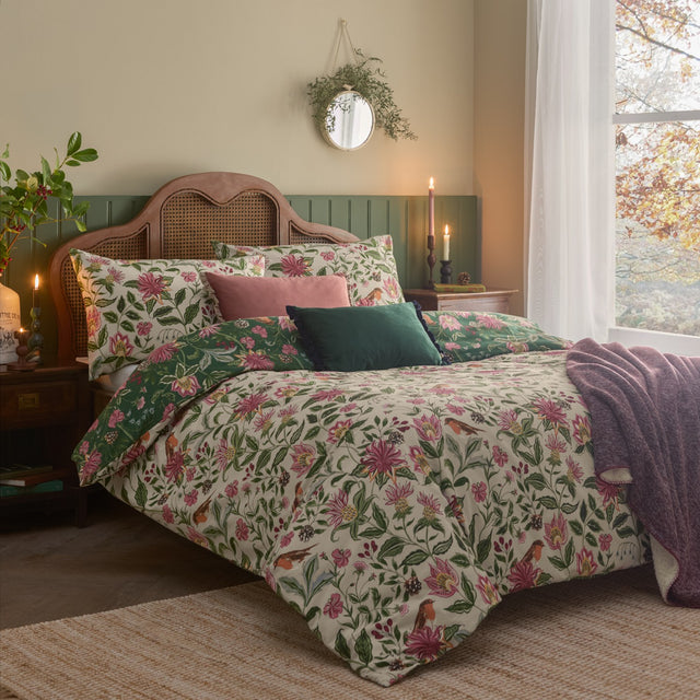 Beatrice Reversible Floral Duvet Cover Set in multicolour on a bed, cream side shown with pink and green botanical print, robin motif and matching pillowcases in a cosy bedroom setting.