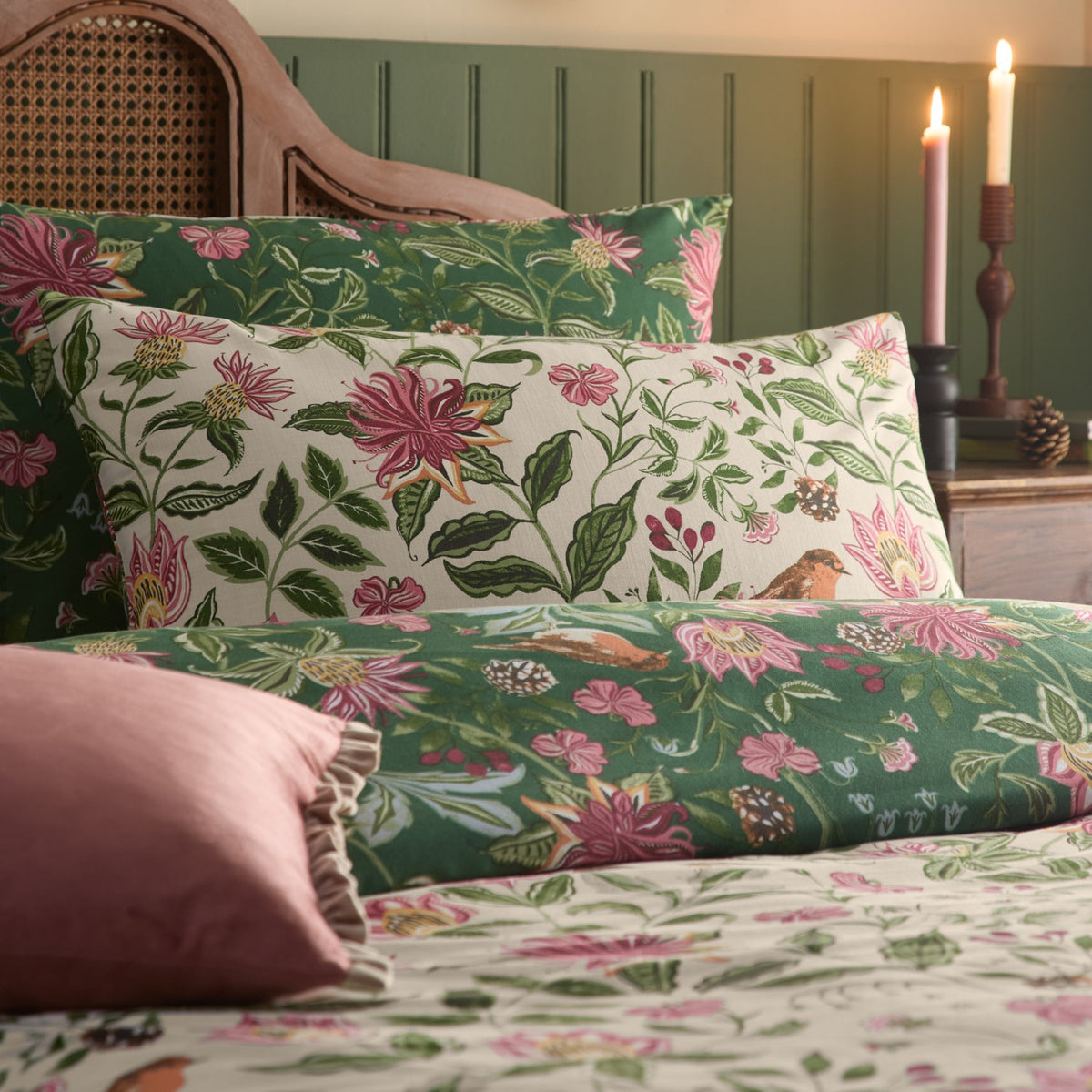 Beatrice Reversible Floral Duvet Cover Set styled on a bed, showing cream and green botanical print pillowcases with pink florals, birds, and a rolled bolster, in a rustic bedroom setting.