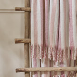 Beechwood striped cotton throw in ivory, pink, and dusky rose with twisted fringe, draped over a wooden ladder rack against a neutral wall.