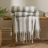 Beechwood Striped Cotton Throw in Heath, cream and grey striped throw with fringed edges, folded and draped over a wooden bench in a living room setting.