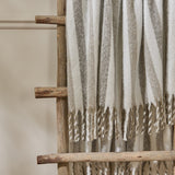 Beechwood Striped Cotton Throw in Heath draped over a wooden ladder rack, showing cream fabric with grey and greige vertical stripes and twisted fringe trim.