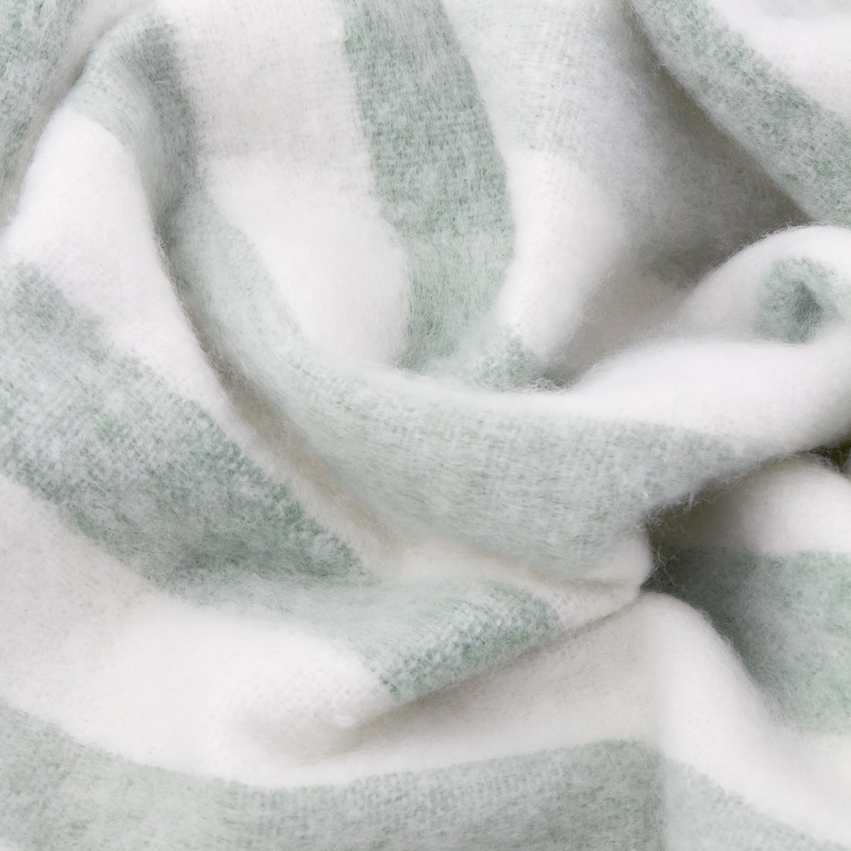 Close-up of the Beechwood Striped Cotton Throw in Moorland Green, showing its brushed, fringed cotton texture with soft sage green and off-white vertical stripes.