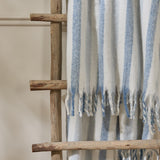 Beechwood Striped Polyester Throw in sky blue and cream, with fringed edges, draped over a wooden ladder against a neutral wall.