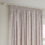 Bella fully lined cotton pencil pleat curtains in natural, showing white floral outline print on a neutral ground, hung from a white pole with curtain hooks near a window.