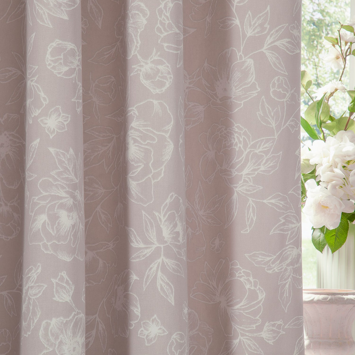Bella Cotton Fully Lined Eyelet Curtain in natural, showing white floral line-work on a soft pink-toned cotton fabric, styled near a window with white flowers.