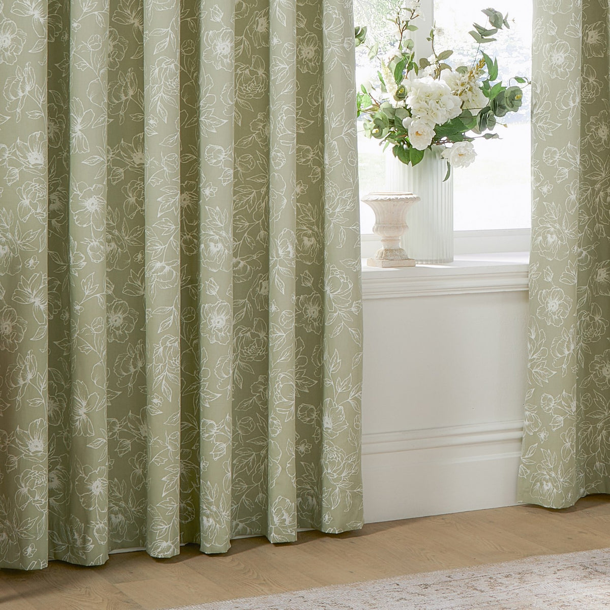 Bella Cotton Fully Lined Eyelet Curtains in Sage, showing eyelet-headed panels with a white line-drawn floral peony print, styled beside a window with a vase of flowers.