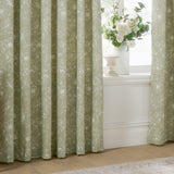 Bella Cotton Fully Lined Eyelet Curtains in Sage, showing eyelet-headed panels with a white line-drawn floral peony print, styled beside a window with a vase of flowers.