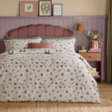 Evergreen Belle Stripe reversible bows duvet cover set with green floral pillowcases and leaf print, styled on a bed with pink headboard in a room with mauve panelling.