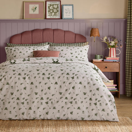 Evergreen Belle Stripe reversible bows duvet cover set with green floral pillowcases and leaf print, styled on a bed with pink headboard in a room with mauve panelling.