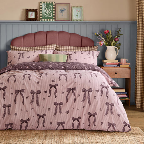 Belle Stripe Reversible Bows Duvet Cover Set in Rosewood, shown styled on a bed with pink pinstripe fabric featuring purple bow and floral print, paired with a striped headboard in a bedroom setting.