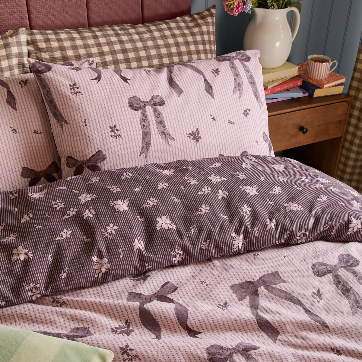 Belle Stripe Reversible Bows Duvet Cover Set in Rosewood, showing pink bow-print pinstripe side and reverse deep purple ditsy floral side with matching pillowcases.