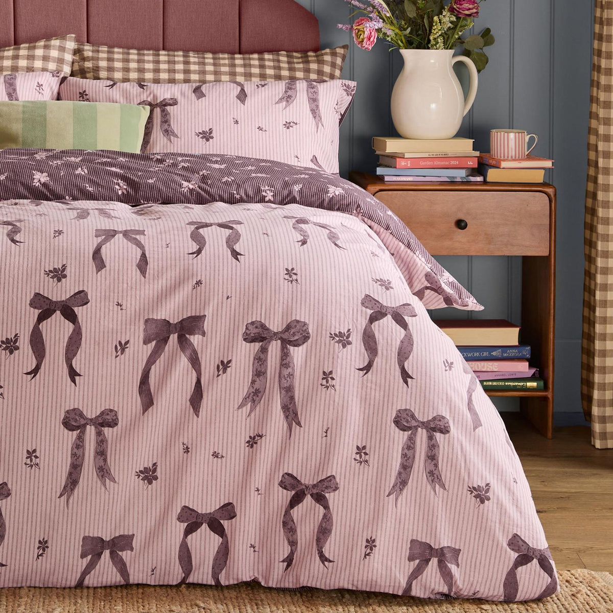 Belle Stripe Reversible Bows Duvet Cover Set in Rosewood, pink pinstripe fabric with purple bow and floral print, shown on a bed with matching pillowcases and striped headboard.