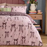 Belle Stripe Reversible Bows Duvet Cover Set in Rosewood, pink pinstripe fabric with purple bow and floral print, shown on a bed with matching pillowcases and striped headboard.