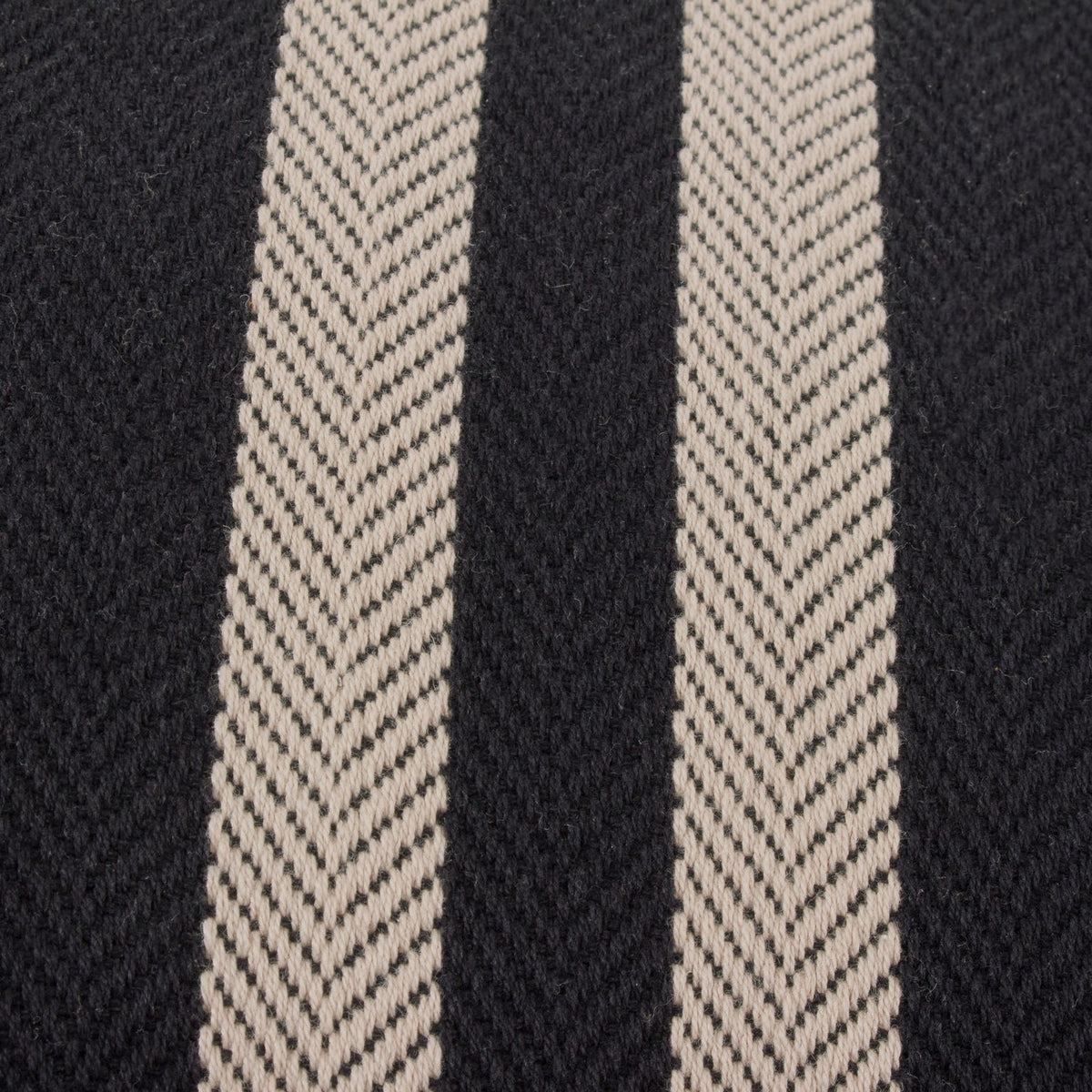 Close-up of the Benton Herringbone Cotton Cushion in black, showing woven herringbone twill texture with two off-centre pale stripes on a black cotton ground.