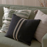 Benton Herringbone Cotton Cushion in black with off-centre pale stripes, shown on a sage green sofa alongside striped and textured neutral cushions.