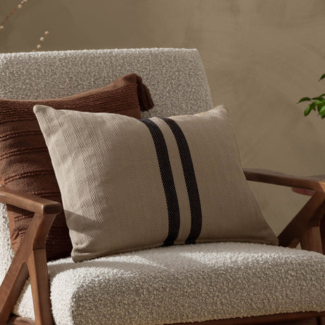 Benton Herringbone Cotton Cushion in natural beige with two dark contrast stripes, shown on a boucle armchair beside a brown textured cushion.