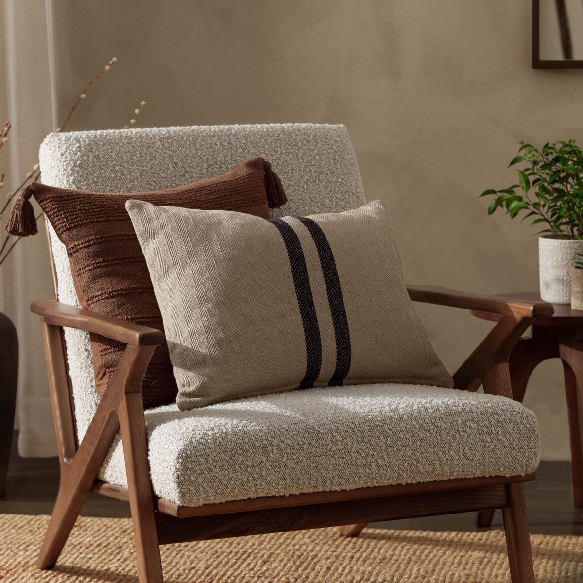 Benton Herringbone Cotton Cushion in natural beige with dark contrast centre stripes, styled on a boucle armchair beside a brown textured cushion.