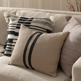 Benton Herringbone Cotton Cushion in natural beige with two dark centre stripes, shown on a sofa alongside patterned and textured scatter cushions.