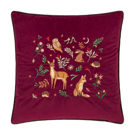 Square burgundy velvet cushion with dark piping, embroidered with a woodland scene featuring an owl, hare, fox, fawn and hedgehogs among leaves and stars.