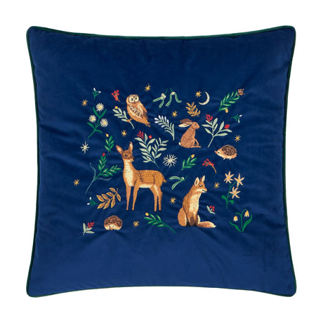 Berry Woods square navy velvet cushion with embroidered woodland scene of owl, hare, deer, fox and hedgehogs among leaves, berries and stars, dark green piped edge, on a white background.
