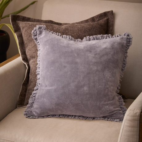 Bertie Velvet Cotton Cushion in mauve with a plain velvet face and frayed fringe edge, shown on a beige armchair with a brown cushion behind.