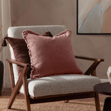Bertie Velvet Cotton Cushion in rose pink with ruffled edging, shown on a boucle armchair with a brown textured cushion in a living room setting.