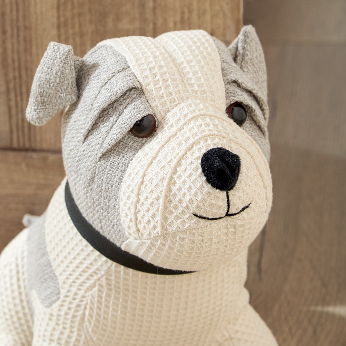 Close-up of the Bestie Dog Waffle Cotton Door Stop in natural, showing its bulldog-style face with grey ear and coat markings, black collar, and stitched muzzle detail.