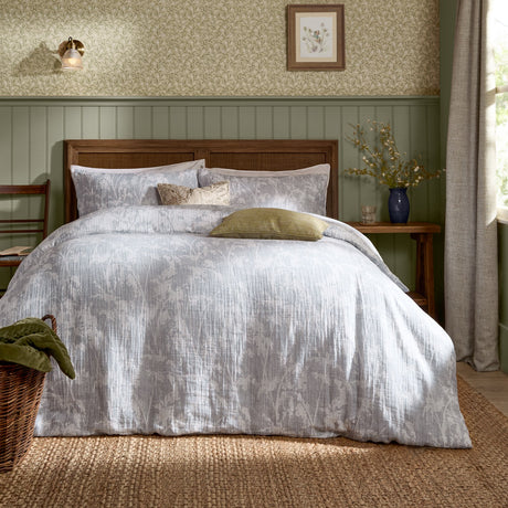 Braeflower Cotton Floral Duvet Cover Set in Chambray dressed on a bed with grey and cream botanic print, styled with cushions in a green-panelled bedroom.