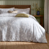Braeflower Cotton Floral Duvet Cover Set in Chambray on a bed with matching pillowcases, styled with patterned and olive cushions in a bedroom with wood-panelled walls.
