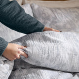 Braeflower Cotton Floral Duvet Cover Set in Chambray, showing grey and cream botanic print cotton fabric being arranged by hand on a bed.
