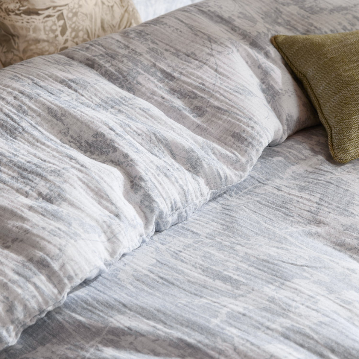 Braeflower Cotton Floral Duvet Cover Set in Chambray, close-up of crinkled grey and white muslin fabric with meadow toile print, styled with olive green and cream cushions.