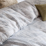 Braeflower Cotton Floral Duvet Cover Set in Chambray, close-up of crinkled grey and white muslin fabric with meadow toile print, styled with olive green and cream cushions.