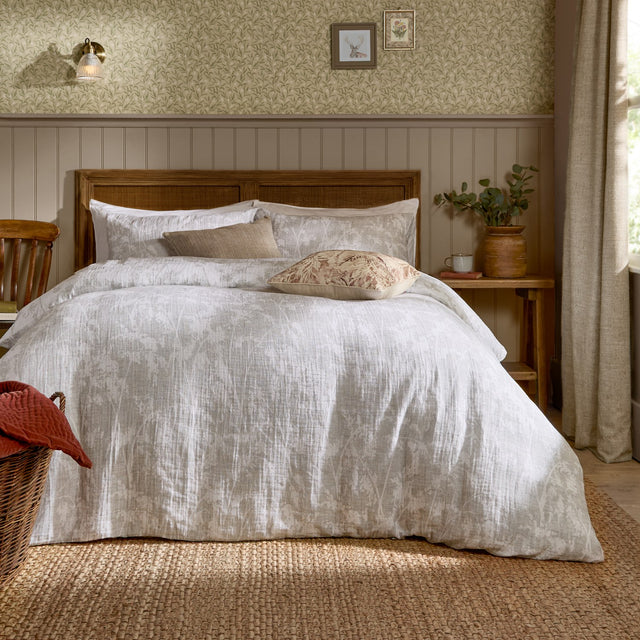 Braeflower Cotton Floral Duvet Cover Set in natural on a wooden bed with cushions, styled in a bedroom with panelled walls and floral wallpaper.