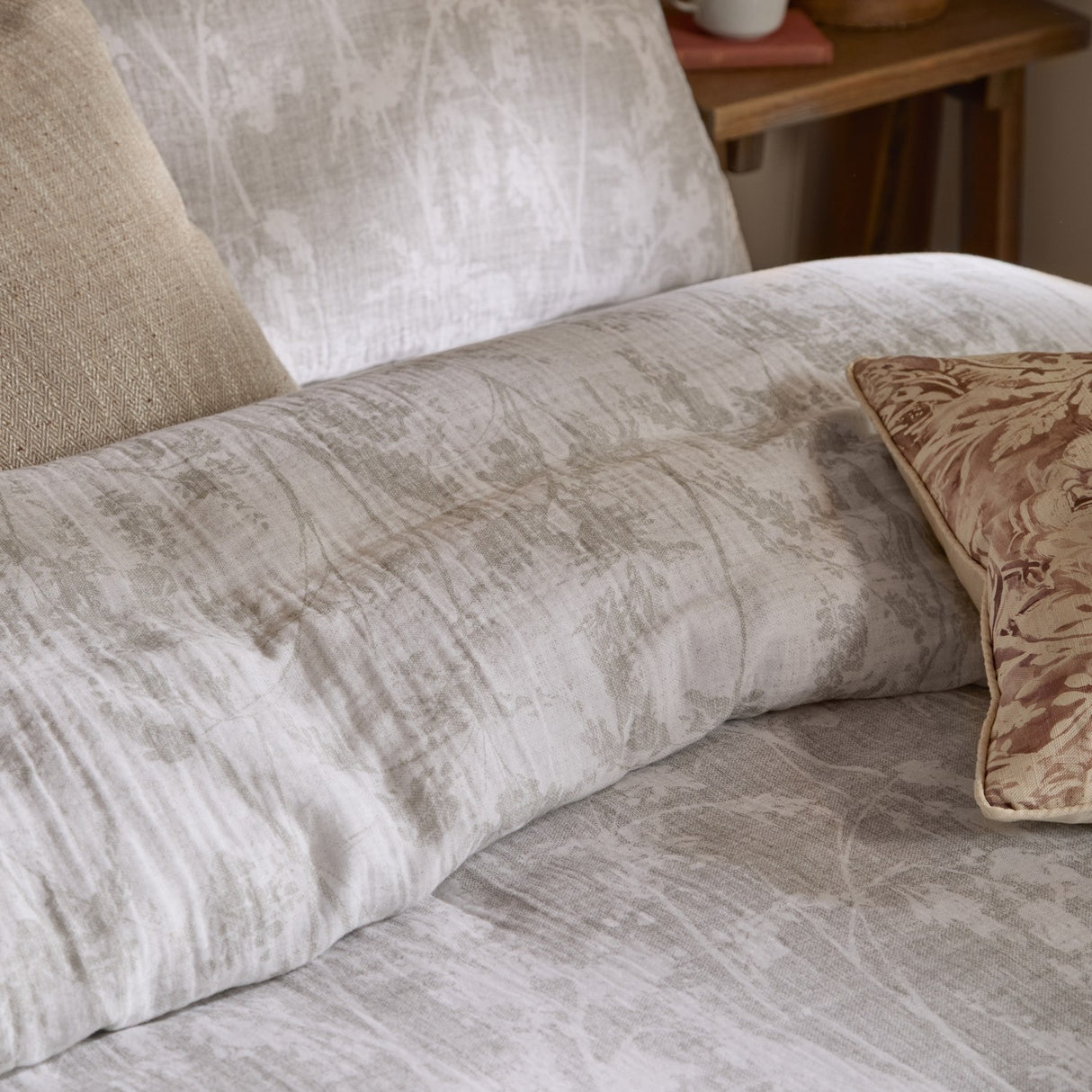 Braeflower Cotton Floral Duvet Cover Set in natural, showing crinkled cotton muslin with a soft meadow toile print, styled with linen and patterned cushions on a bed.