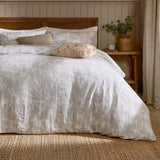 Braeflower Cotton Floral Duvet Cover Set in natural, with crinkled muslin fabric and a meadow toile print, styled on a bed beside a rattan headboard and wooden nightstand.