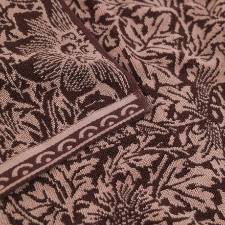 Close-up of the Bird and Anemone Floral Cotton Bath Mat in plum, showing the two-tone woven bird and leaf pattern with a decorative scalloped border edge.