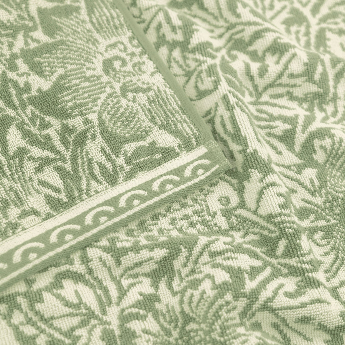 Close-up of the Bird and Anemone Floral Cotton Bath Mat in sage green, showing the woven botanical pattern with birds, anemone flowers and foliage, edged with a scrolled border.