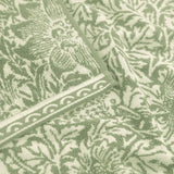 Close-up of the Bird and Anemone Floral Cotton Bath Mat in sage green, showing the woven botanical pattern with birds, anemone flowers and foliage, edged with a scrolled border.