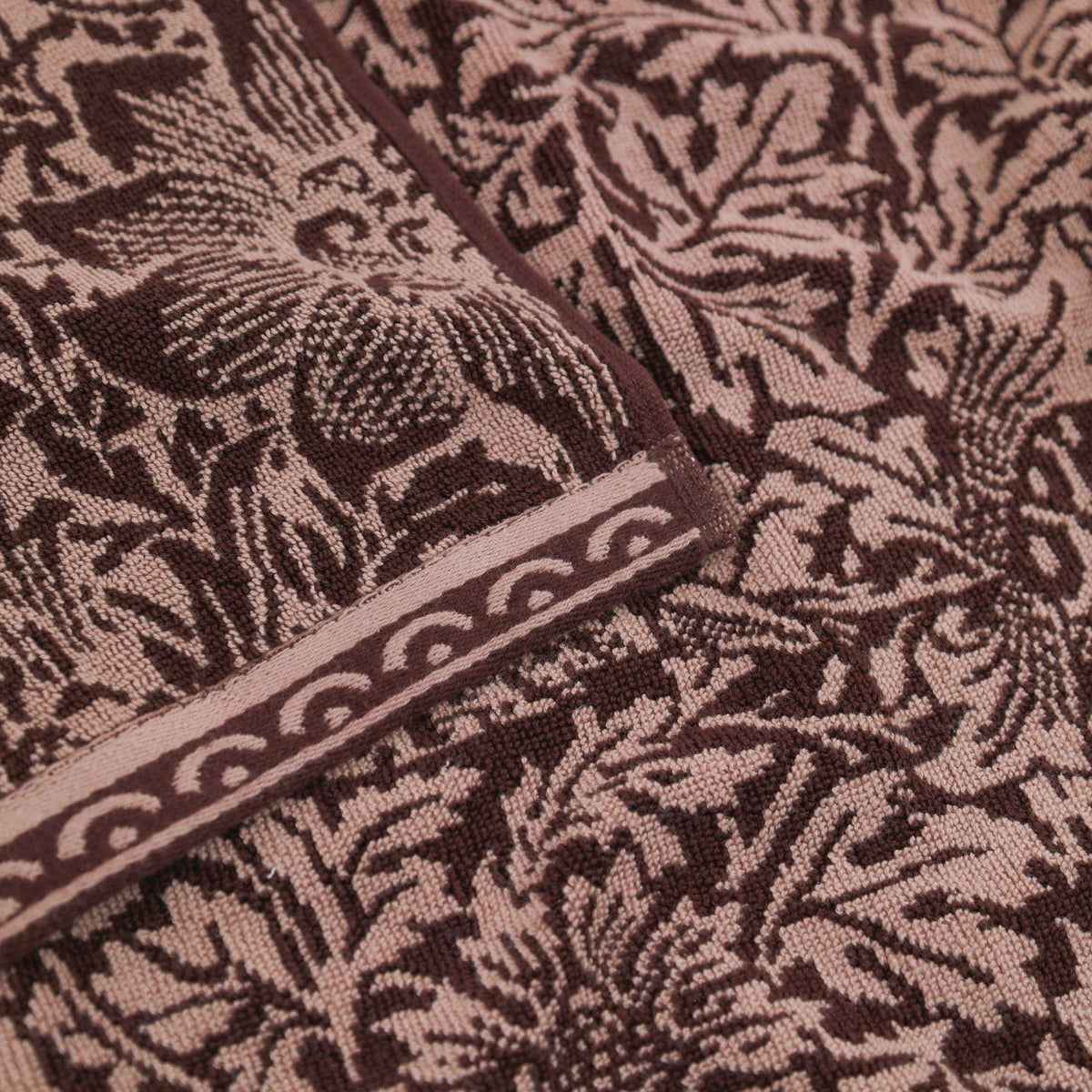Close-up of the Bird & Anemone Jacquard Cotton Towel in plum, showing the woven bird and floral pattern in aubergine and dusky rose with a scalloped border trim.