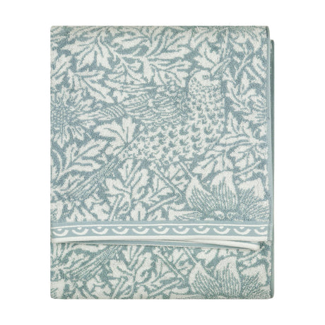 Folded Bird & Anemone jacquard cotton towel in slate blue with woven bird and foliage pattern and scalloped border trim, shown on a plain white background.