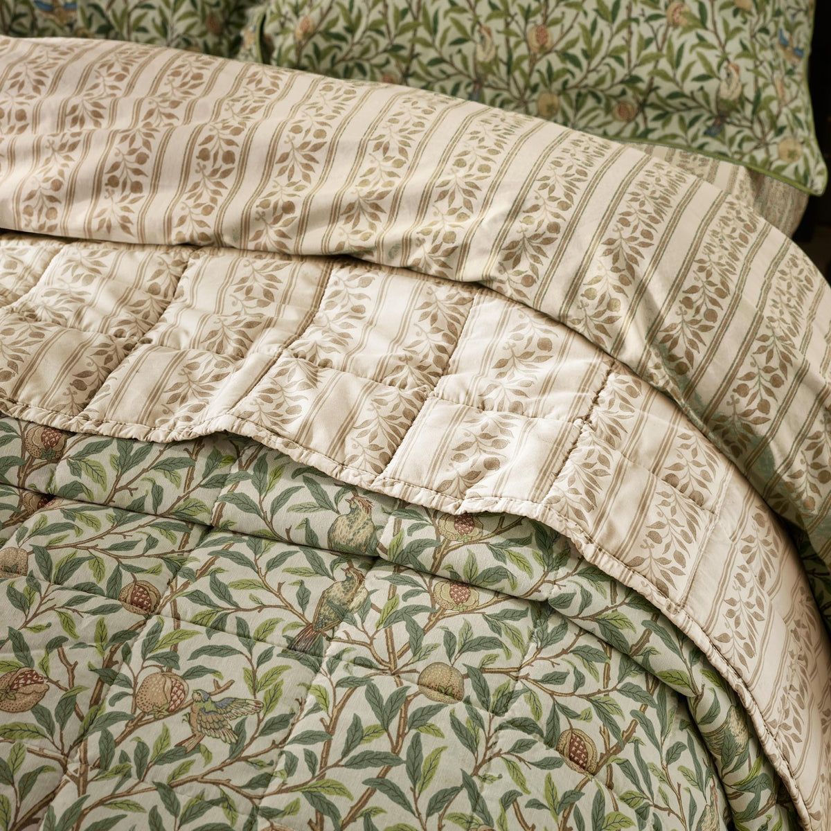 Quilted cotton bedspread with Bird & Pomegranate design in herbal green, folded back to reveal a striped cream and beige percale reverse and pillow shams behind.