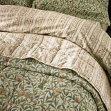 Quilted cotton bedspread with Bird & Pomegranate design in herbal green, folded back to reveal a striped cream and beige percale reverse and pillow shams behind.