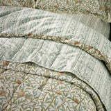 Quilted Bird & Pomegranate cotton bedspread in sage, showing the bird and pomegranate print folded back to reveal the leafy striped reverse side.
