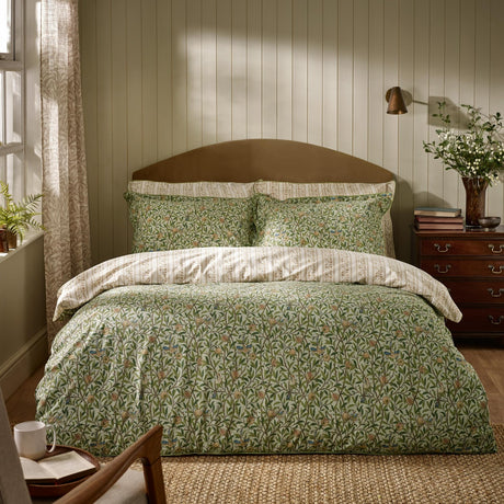 Bird & Pomegranate cotton floral duvet cover set in herbal green with matching pillowcases, styled on a bed with a brown headboard in a panelled bedroom.